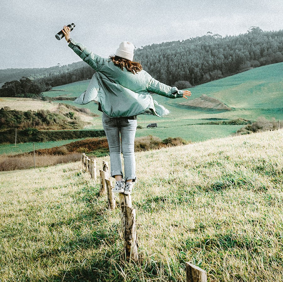 Bild einer jungen Person, die auf einem alten Zaunpfahl vor einer wunderbaren Naturlandschaft balanciert.
